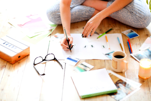 Young woman with art supplies preparing a project on the wood floor.