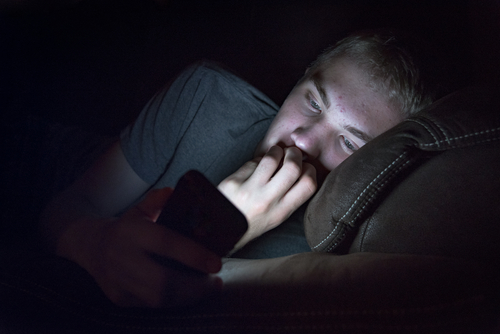 Depressed teenage boy on his phone in bed.